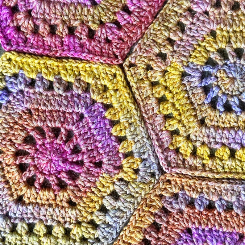 May include: Close-up of a crocheted blanket with a multi-colored pattern of pink, purple, yellow, and orange. The blanket is made of yarn and has a textured surface.