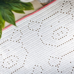 May include: White crochet blanket with a pink border and a geometric pattern.