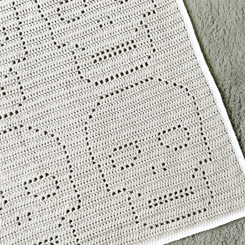 Pu&ograve; includere: Una coperta all'uncinetto con un bordo bianco e un motivo a rombi. La coperta &egrave; realizzata con un filato grigio chiaro.