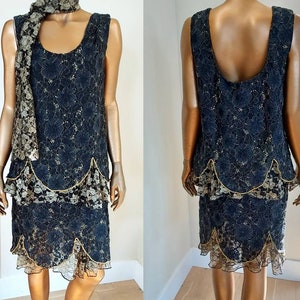 May include: A black lace dress with gold accents and a scalloped hemline. The dress has a sleeveless design and a fitted silhouette.
