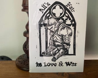 May include: A black and white print of a kneeling knight in full armor, set within a gothic arch design. The text "All's Fair in Love & War" is printed below the knight. The print is on a white background.