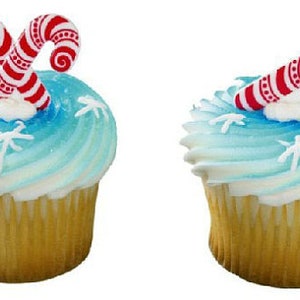 May include: Two cupcakes with blue frosting and white snowflake sprinkles. Each cupcake is topped with a red and white candy cane.