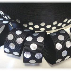 Puede incluir: Cinta de grosgrain negra con lunares plateados. La cinta está enrollada y los lunares son visibles en el borde del rollo.