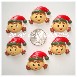 May include: Six red and green elf-themed Christmas ornaments with brown hair and smiling faces. The ornaments are approximately the size of a US quarter.