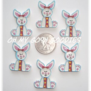 May include: Seven white bunny-shaped embellishments with pink ears and bows, blue outlines, and red and yellow accents. The text "OH MY GOSH GOODIES" is visible. A quarter is included for size reference.