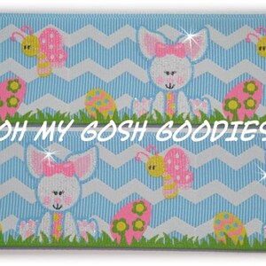 May include: Blue and white chevron ribbon with a repeating pattern of pink and white bunnies, yellow butterflies, and pink and yellow Easter eggs. The ribbon has a glittery finish. "Oh My Gosh Goodies" is printed on the ribbon.