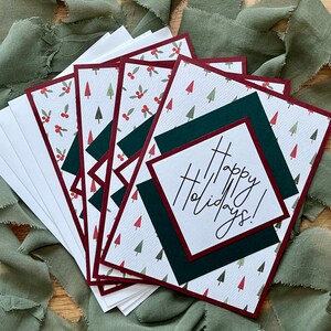 Puede incluir: Conjunto de cinco tarjetas navideñas con fondo blanco, árboles verdes y bayas rojas. Las tarjetas tienen un borde burdeos y un cuadrado verde con un borde burdeos que dice "¡Felices Fiestas!" en cursiva blanca.