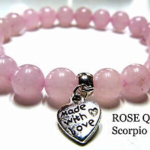 May include: A pink rose quartz bracelet with a silver heart charm that says "made with love". The bracelet is labeled "ROSE QUARTZ Scorpio".