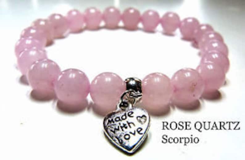 May include: A pink rose quartz bracelet with a silver heart charm that says "made with love". The bracelet is labeled "ROSE QUARTZ Scorpio".