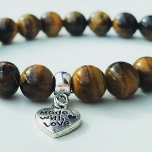 May include: A brown and gold tiger's eye beaded bracelet with a silver heart charm that says "Made with Love".