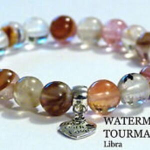 May include: Watermelon tourmaline bracelet with pink, clear, and brown beads and a silver heart charm. The bracelet has a "WATERMELON TOURMALINE" label and says "Libra".