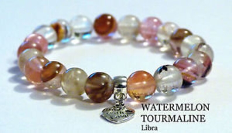 May include: Watermelon tourmaline bracelet with pink, clear, and brown beads and a silver heart charm. The bracelet has a "WATERMELON TOURMALINE" label and says "Libra".