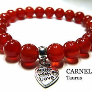 May include: Red carnelian gemstone bracelet with a silver heart charm that says "Made with Love". The bracelet is labeled "CARNELIAN Taurus".