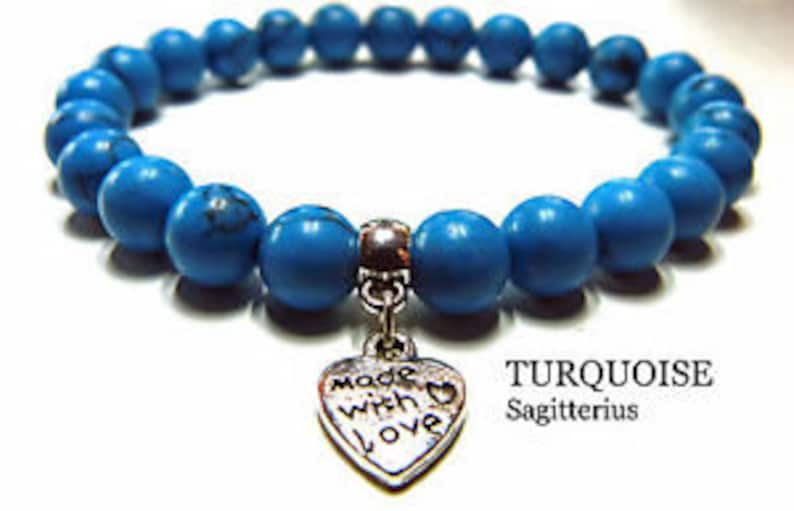May include: Turquoise blue beaded bracelet with a silver heart charm that says "made with love". The bracelet is labeled "TURQUOISE Sagittarius".