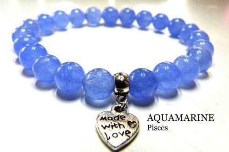 May include: A light blue aquamarine gemstone bracelet with a silver heart charm that says "Made with Love". The bracelet is labeled "Aquamarine Pisces".