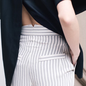 May include: White striped pants with a black shirt tucked in. The shirt has a V-shaped opening in the back.