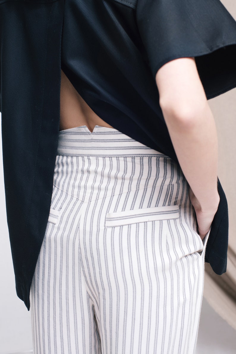 May include: White striped pants with a black shirt tucked in. The shirt has a V-shaped opening in the back.