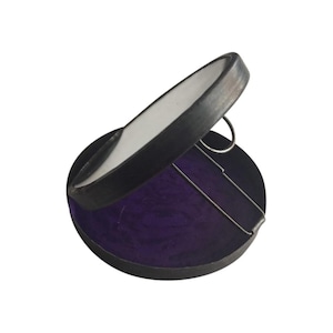 May include: A black compact mirror with a purple velvet lining. The mirror is hinged and opens to reveal a round mirror.