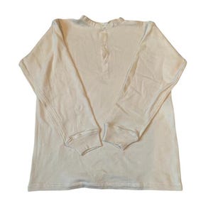 May include: Cream-coloured long-sleeved shirt with a Henley neckline and three buttons. The shirt features ribbed cuffs and a relaxed fit, suitable for casual wear. The fabric appears to be a soft, breathable material.
