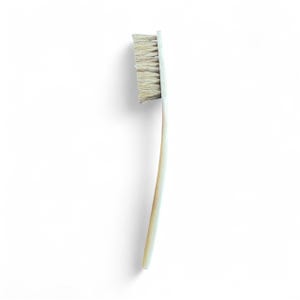 以下が含まれることがあります： 曲がった柄と明るい色の毛が詰まった長方形のヘッドが付いた、明るい色の歯ブラシ。歯ブラシは白い背景に置かれています。
