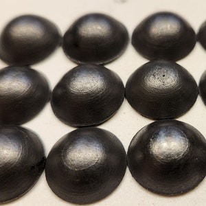 May include: Twelve black metal dome-shaped buttons arranged in a grid pattern on a white surface.