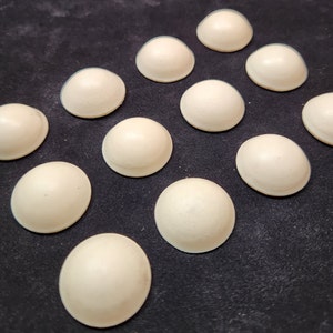 May include: A collection of 12 off-white, round, dome-shaped objects arranged in a diamond pattern on a black surface.