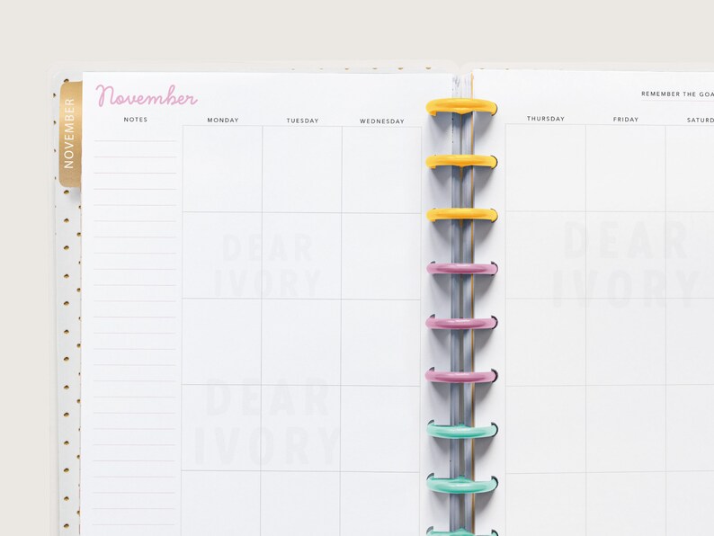 May include: A planner open to a November monthly spread. The page is white with a pink "November" header and a grid for daily planning. The planner has colorful disc binding and a gold polka dot cover.