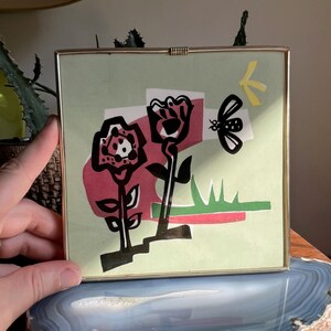 Peut inclure: Un collage encadré de découpages de papier représentant des fleurs stylisées et un papillon. Les fleurs sont rouges, noires et blanches, et le papillon est noir et jaune. L'arrière-plan est de couleur vert clair.