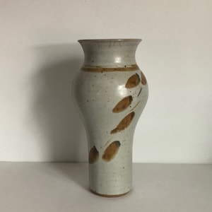 May include: A white ceramic vase with a brown glaze and a leaf design. The vase is tall and slender with a rounded base.