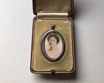 May include: A silver locket containing a portrait of a woman, presented in a brown velvet box with gold edging.