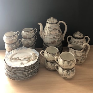 May include: A set of vintage Japanese porcelain teacups, saucers, and teapot with a delicate floral and landscape design. The set includes a creamer and sugar bowl.