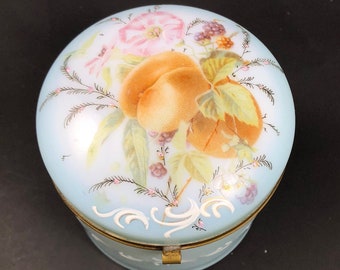May include: A vintage porcelain trinket box with a light blue lid. The lid is decorated with a hand-painted floral design featuring peaches, leaves, and berries.