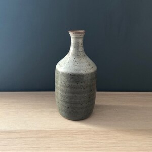May include: A small, grey ceramic vase with a speckled glaze. The vase has a rounded body and a narrow neck.