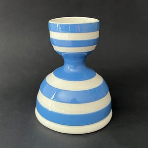 Puede incluir: Un huevero de cerámica con un patrón de rayas azules y blancas. El huevero tiene una base redondeada, una cintura estrecha y una parte superior acampanada. Las rayas azules se alternan con las rayas blancas. Un artículo de cocina decorativo.