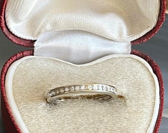 May include: A white gold band ring with small diamonds set in a channel setting. The ring is in a red velvet heart-shaped box with the inscription "M.J.  Jewelle  B. Hogan  Brandtweite  Brown  KENDAL".