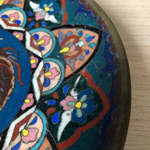 May include: A round, decorative plate with a blue, green, pink, and yellow floral pattern. The plate is made of metal and has a slightly raised rim.
