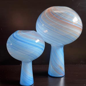 May include: Two glass vases with a spherical top and a stem. The vases are light blue with swirling stripes of blue and orange. The vases are of different sizes, with one taller than the other.