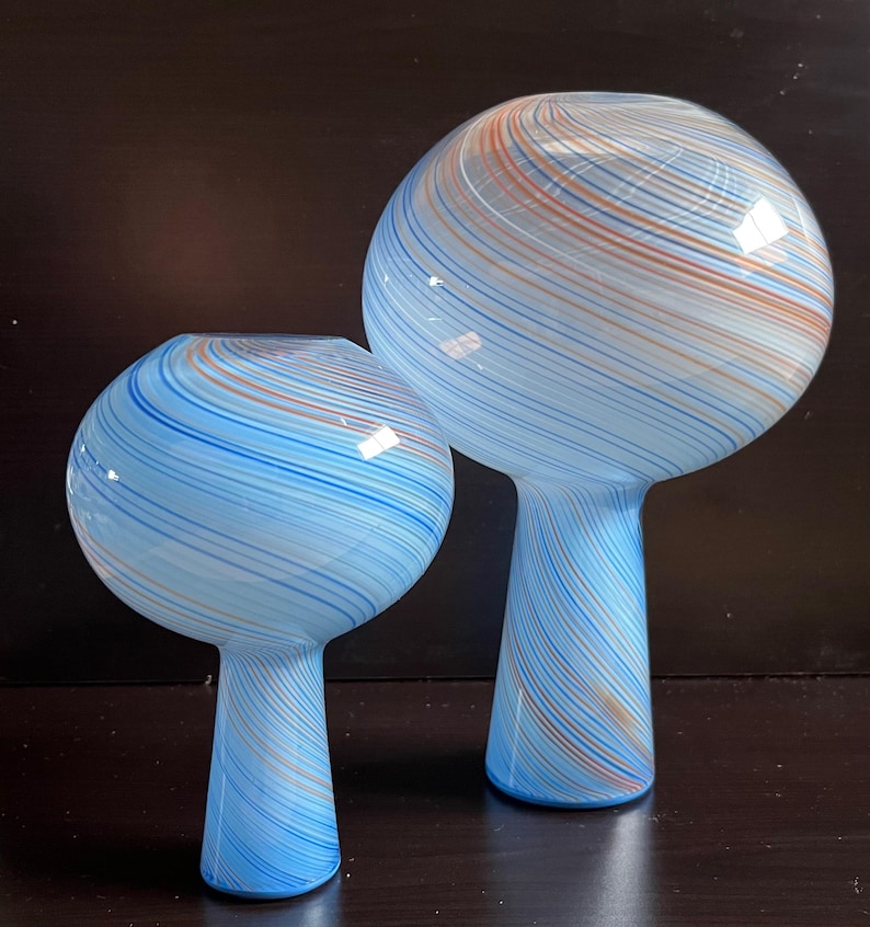 May include: Two glass vases with a spherical top and a stem. The vases are light blue with swirling stripes of blue and orange. The vases are of different sizes, with one taller than the other.