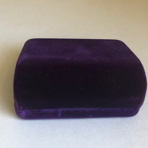 May include: A small, dark purple velvet box. The box is closed and has a smooth, soft surface.