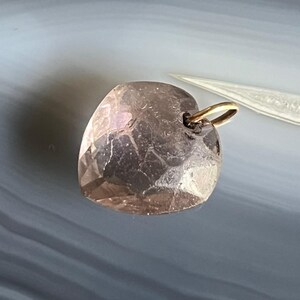 May include: A faceted, heart-shaped pendant in a light brown hue. The pendant has a gold-colored bail for attaching to a chain. The surface of the heart has multiple facets, giving it a textured appearance.