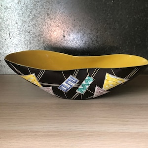 Puede incluir: Un cuenco de cerámica negro con interior amarillo y un diseño geométrico en tonos de amarillo, rosa, azul y verde.