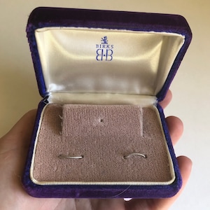 May include: A purple velvet jewelry box with the Birks logo and two silver rings inside.