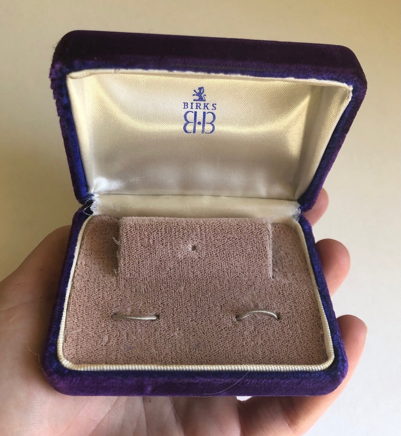 May include: A purple velvet jewelry box with the Birks logo and two silver rings inside.