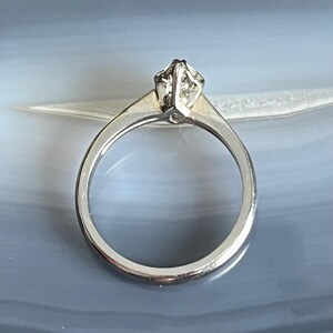 Puede incluir: Un anillo de compromiso de plata con un solo diamante transparente engastado en garras.