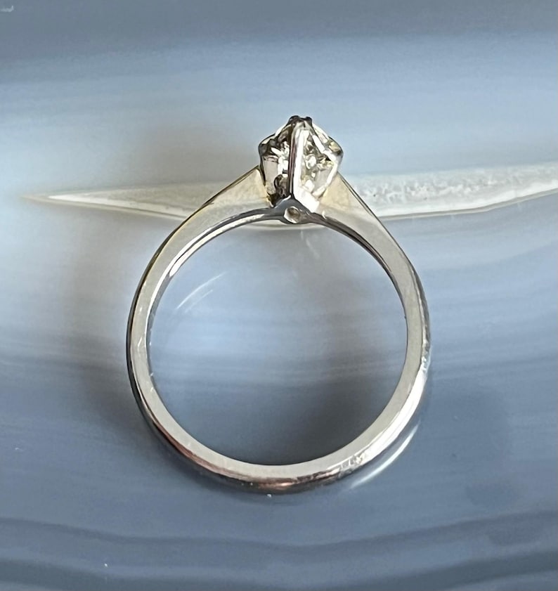 Puede incluir: Un anillo de compromiso de plata con un solo diamante transparente engastado en garras.