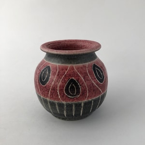 May include: A small, round ceramic vase with a pink and black geometric design. The vase has a wide mouth and a narrow base.
