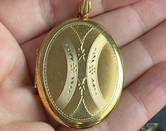 Può includere: Un medaglione ovale in oro con un motivo floreale. Il medaglione ha un coperchio incernierato e un anello per attaccare una catena.