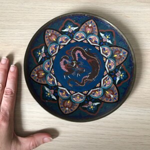 May include: A round, blue and white ceramic plate with a dragon design in the center. The plate is decorated with a colorful floral pattern around the edge.