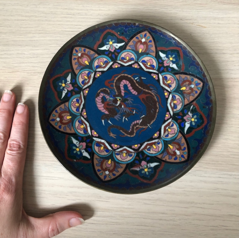 May include: A round, blue and white ceramic plate with a dragon design in the center. The plate is decorated with a colorful floral pattern around the edge.