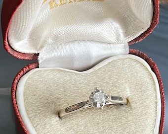 May include: A diamond engagement ring in a red heart-shaped ring box. The box is lined with white velvet and has the inscription "G. Hogg, Brantwaite Brow, KENDAL" on the lid.